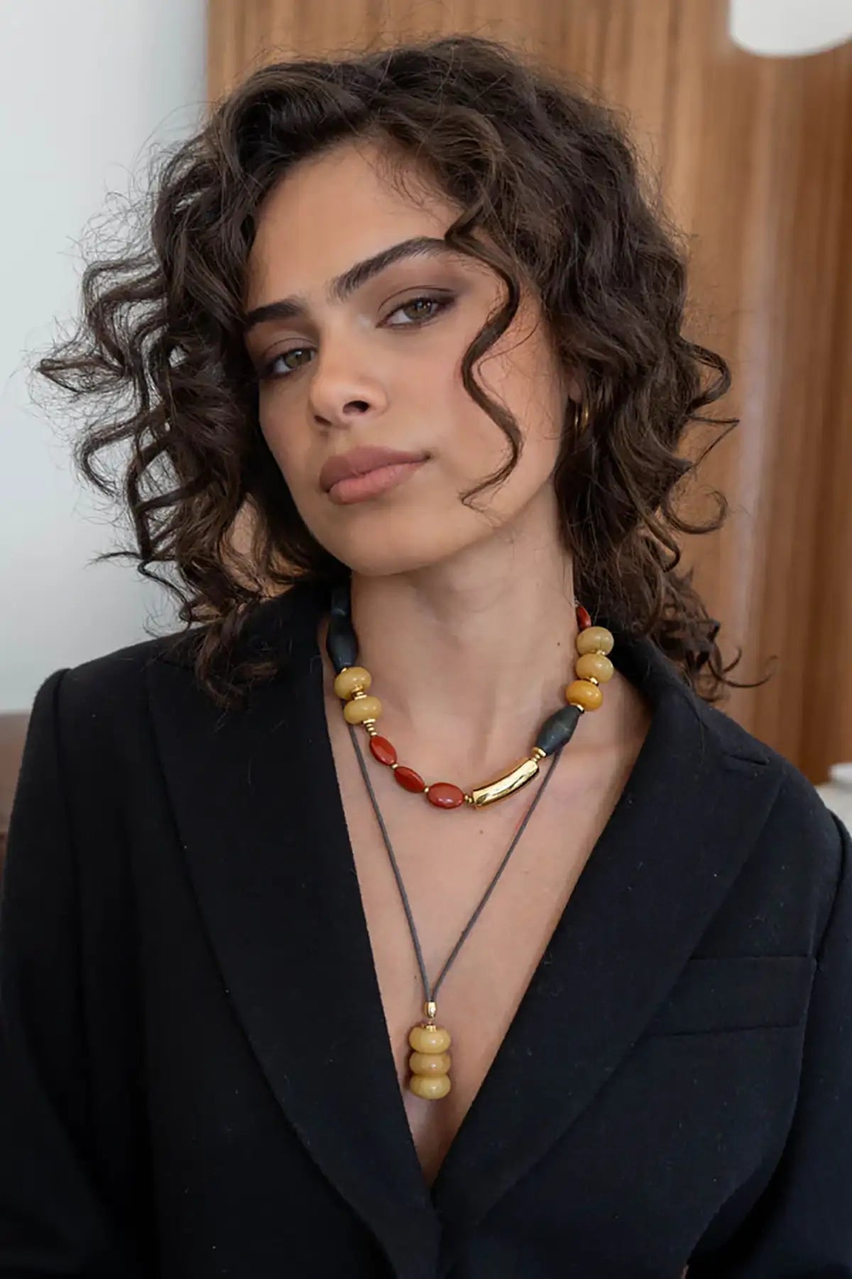 Woman wearing a black suit and colorful beaded necklace against a neutral background