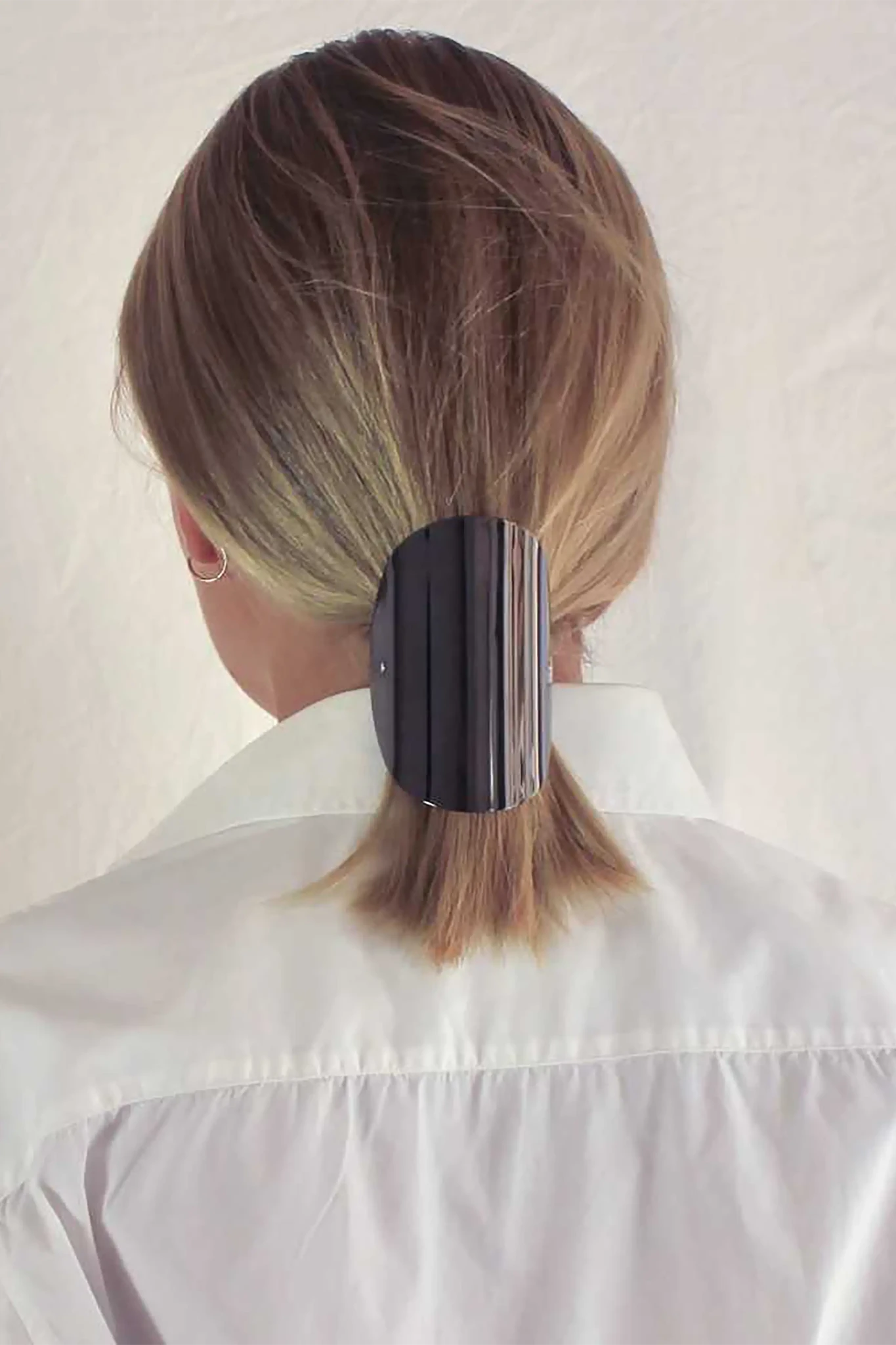Woman with blonde shoulder length hair wearing the Sculpted Arc Barrette on her ponytail against a white background
