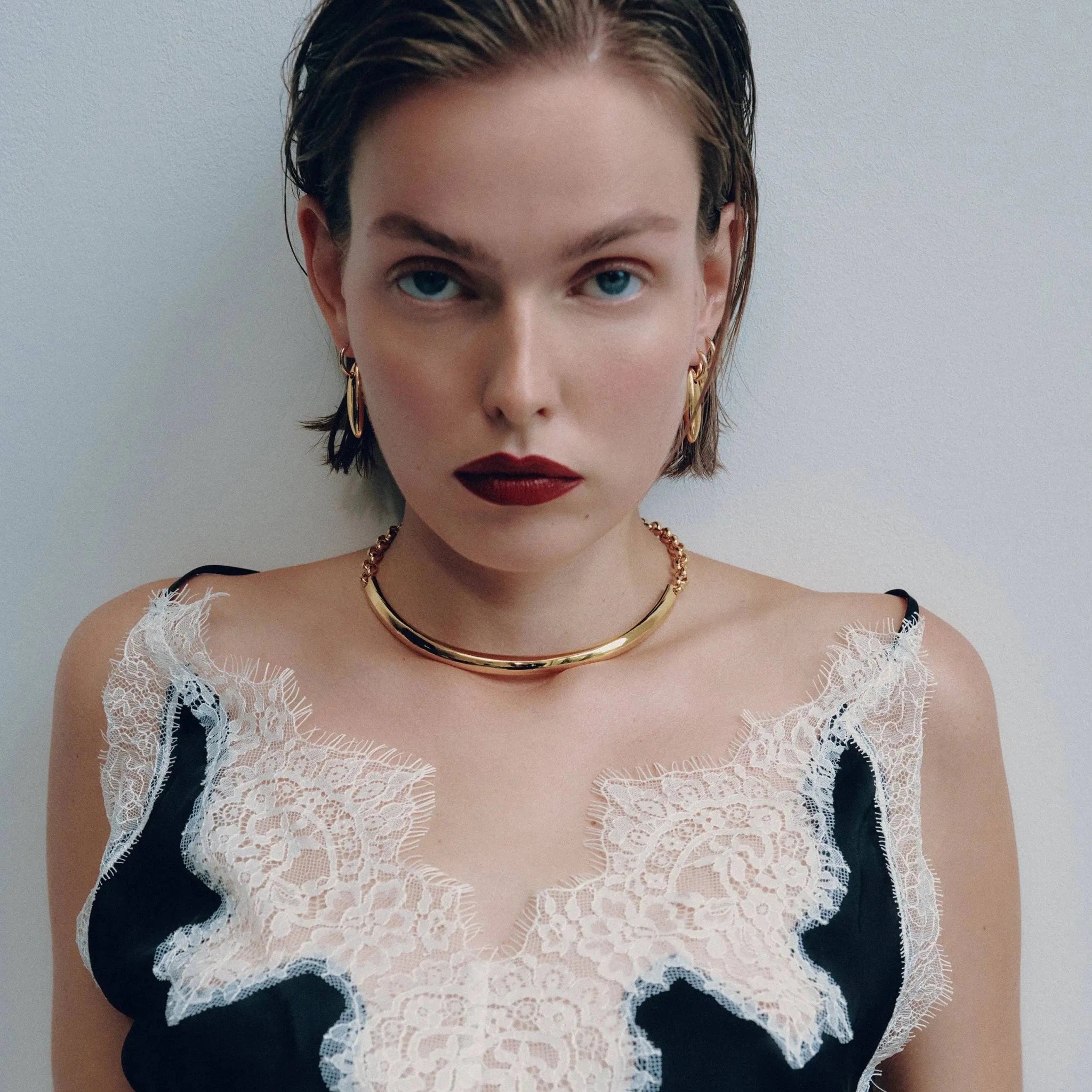 Woman wearing a black and white lace top with gold earrings and the Golden Arc Gold Collar Necklace on light background