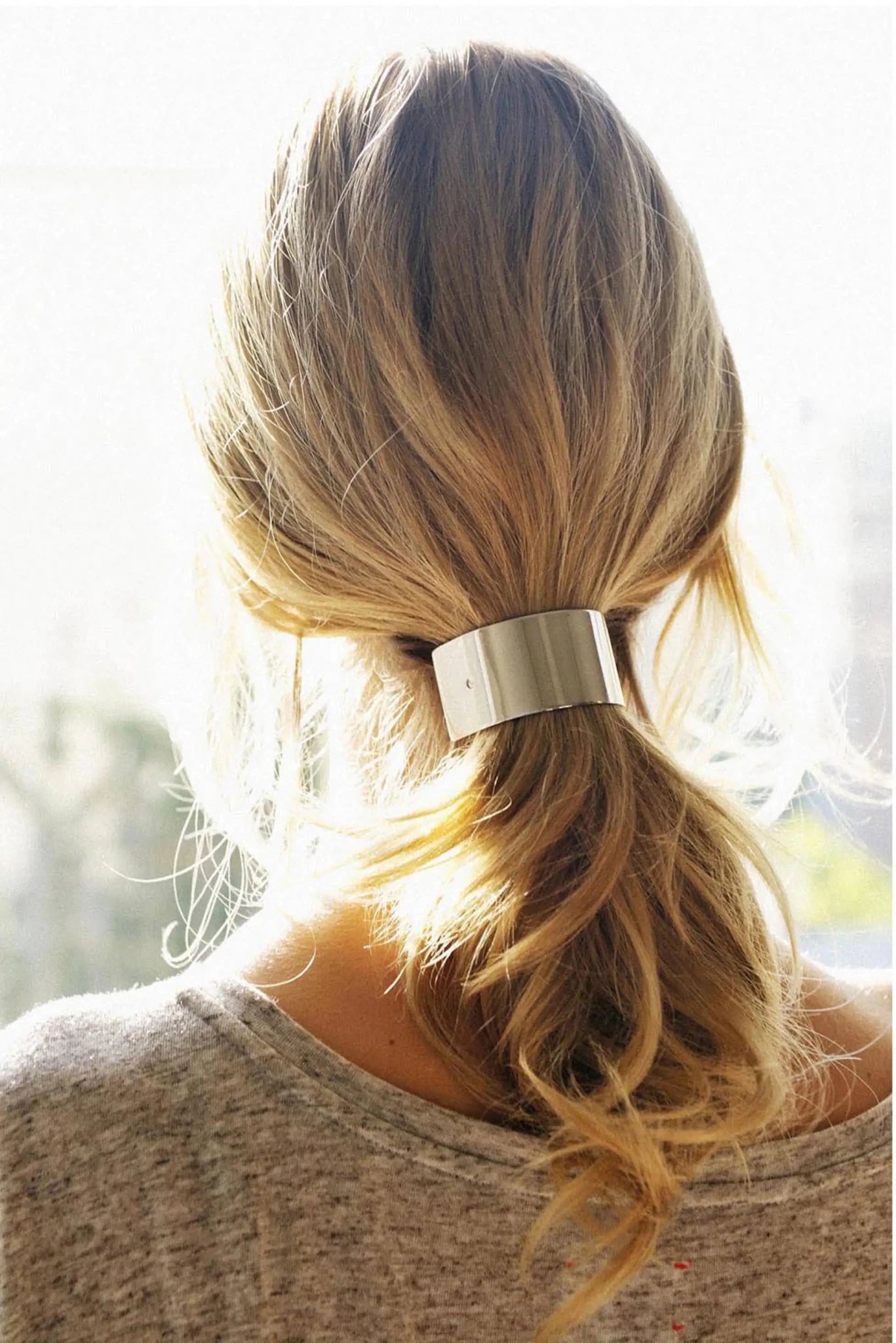 Woman with blonde hair tied in a ponytail with a silver hair barrette, wearing a beige sweater.