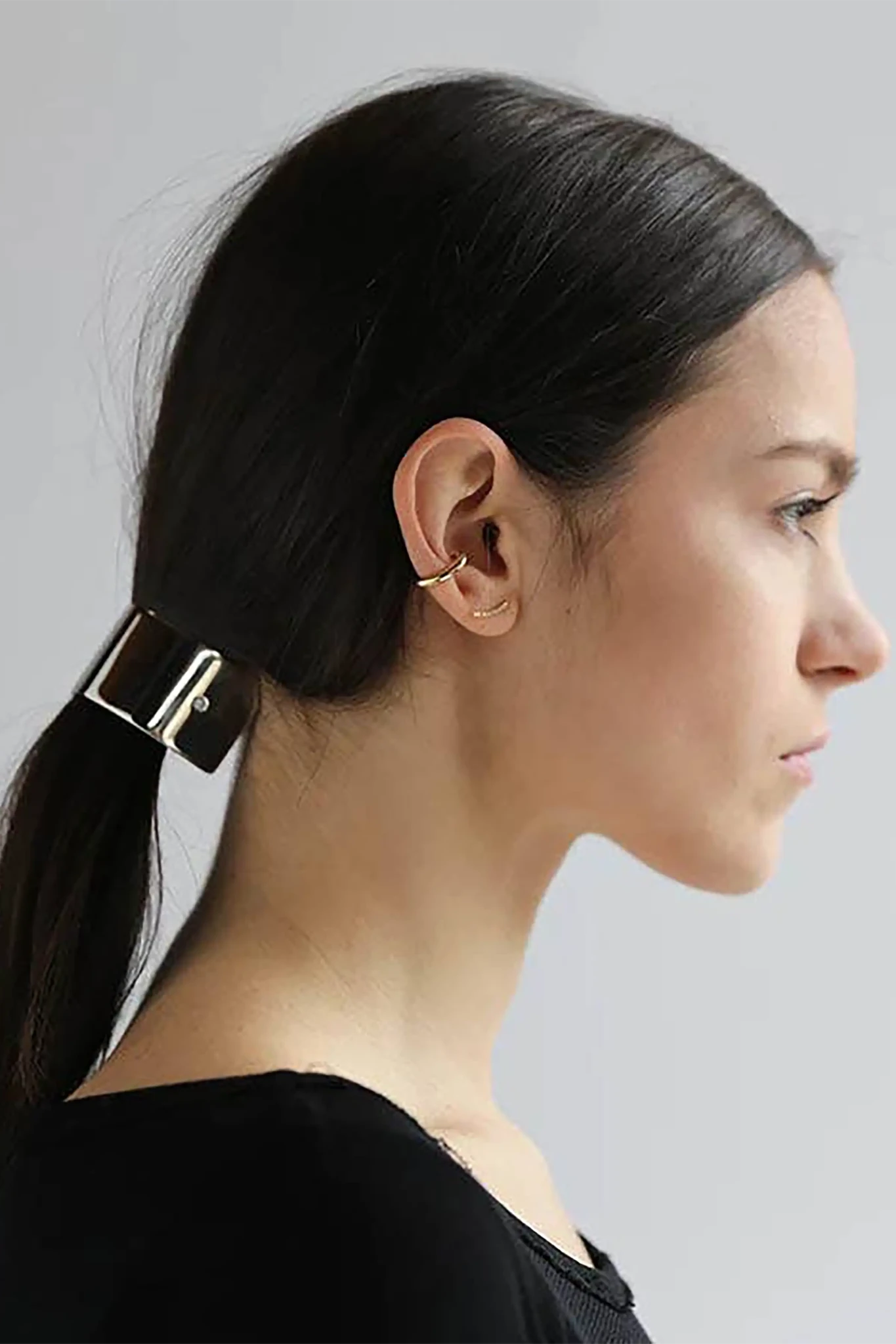 Woman with Sculpted Wide Ponytail Barrette on ponytail wearing a small earring against a plain background