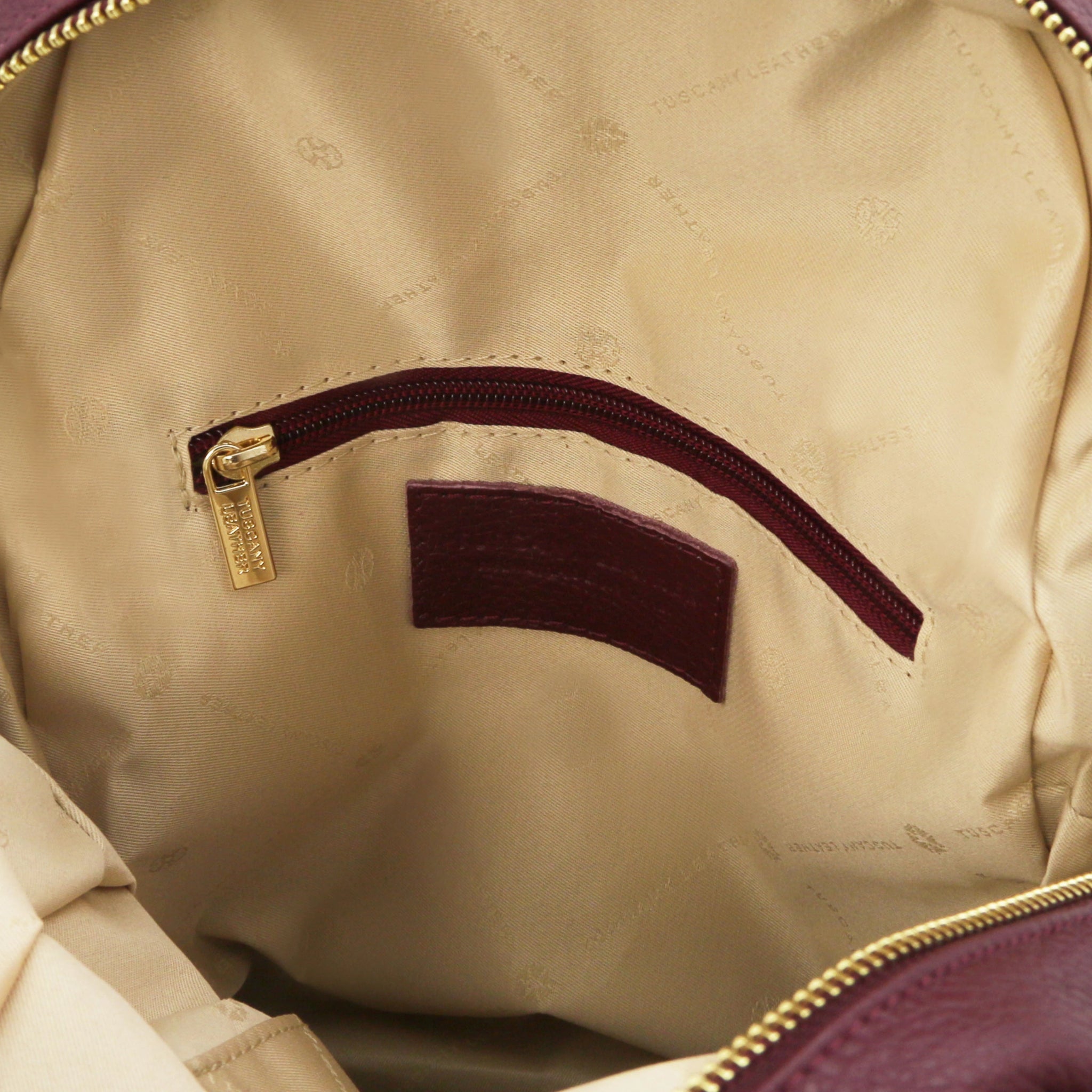 Interior zip pocket with beige lining view of Bordeaux backpack with gold zipper