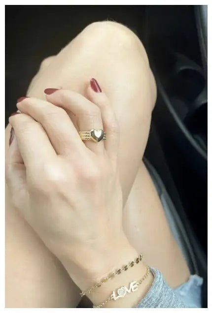 A woman has her legs crosses, wearing the Verona Gratitude Heart Adjustable Ring on right hand, laying on her left knee