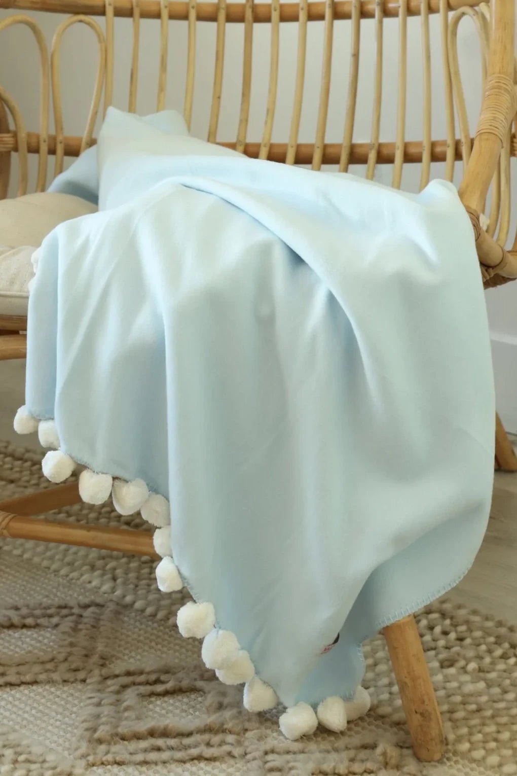 Bamboo Luxxe Pom Pom Throw in baby blue with white pom poms laying in a wooden chair - L'Atelier Global