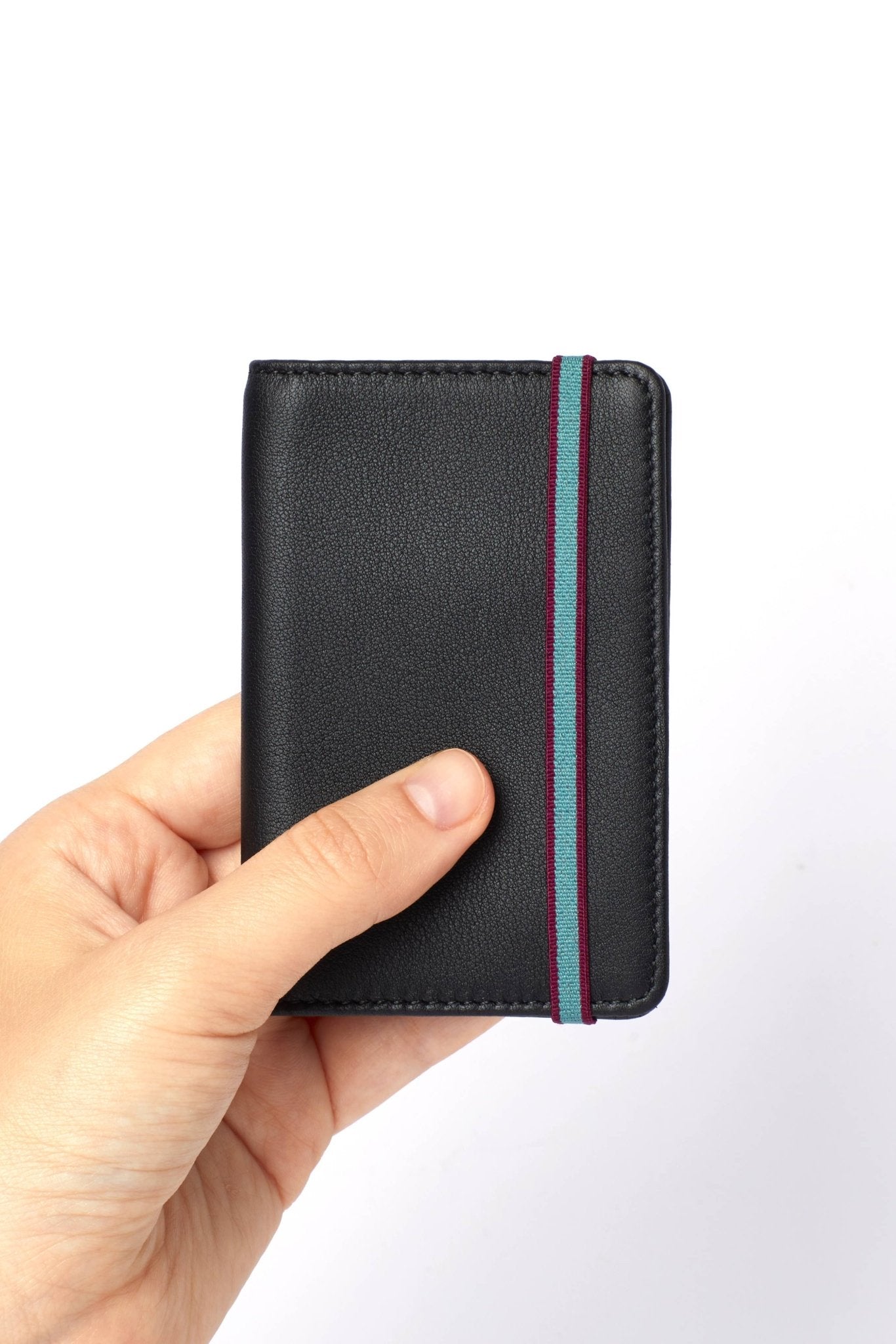 A man's hand holding the Black Leather Card Holder with a blue elastic closure on a white background - L'Atelier Global