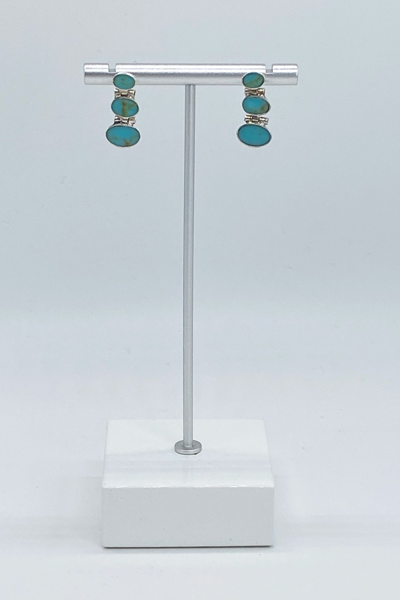 Chilean Turquoise Oval Drop Earrings hanging on a jewelry display with a white marble base - L'Atelier Global