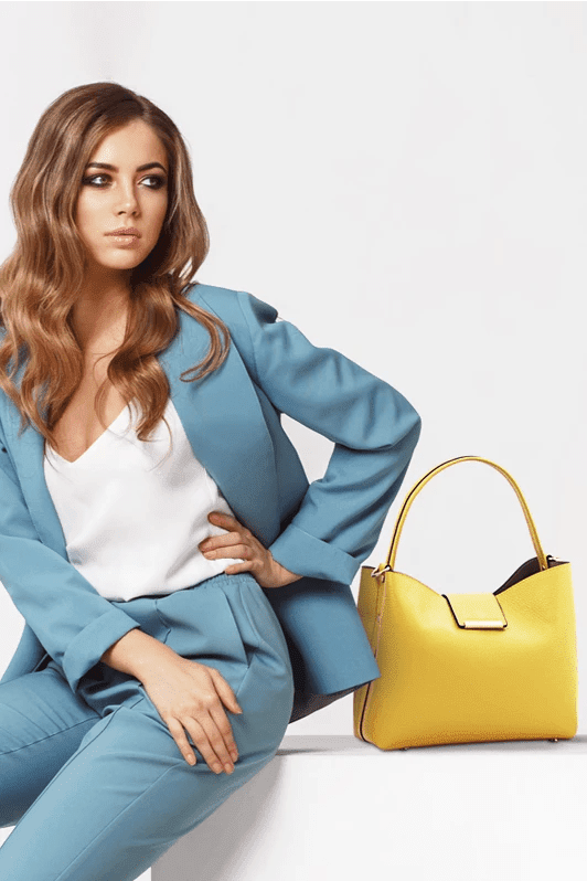 Woman wearing a light blue pant suit sitting next to the Pebbled Leather Secchiello Bag in Pastel Yellow