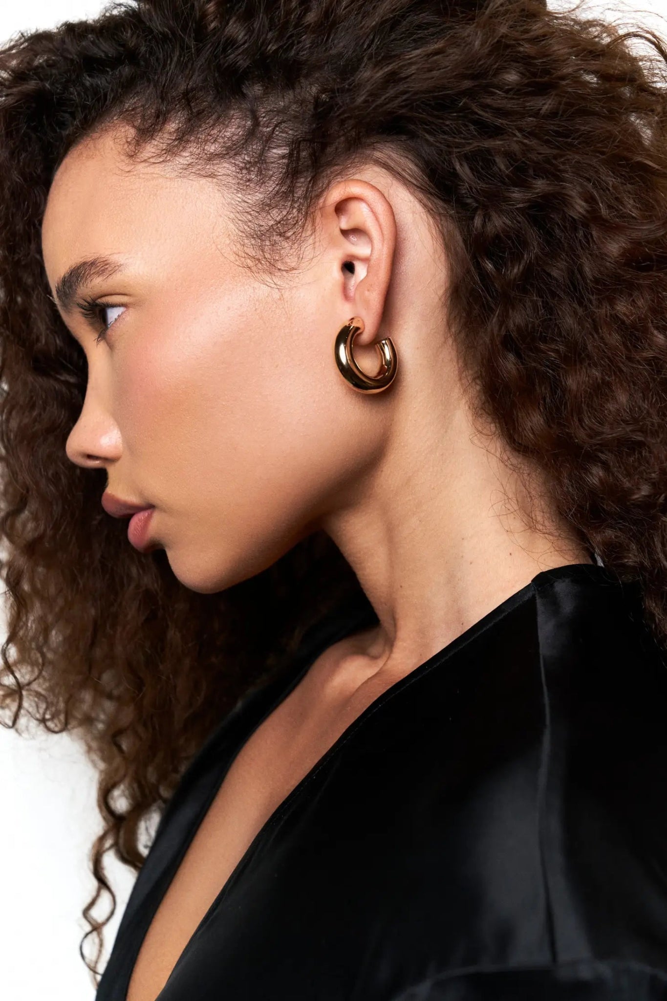 A female model is wearing the Downtown Minimalist Gold Hoops. The image shows her left profile  - L'Atelier Global