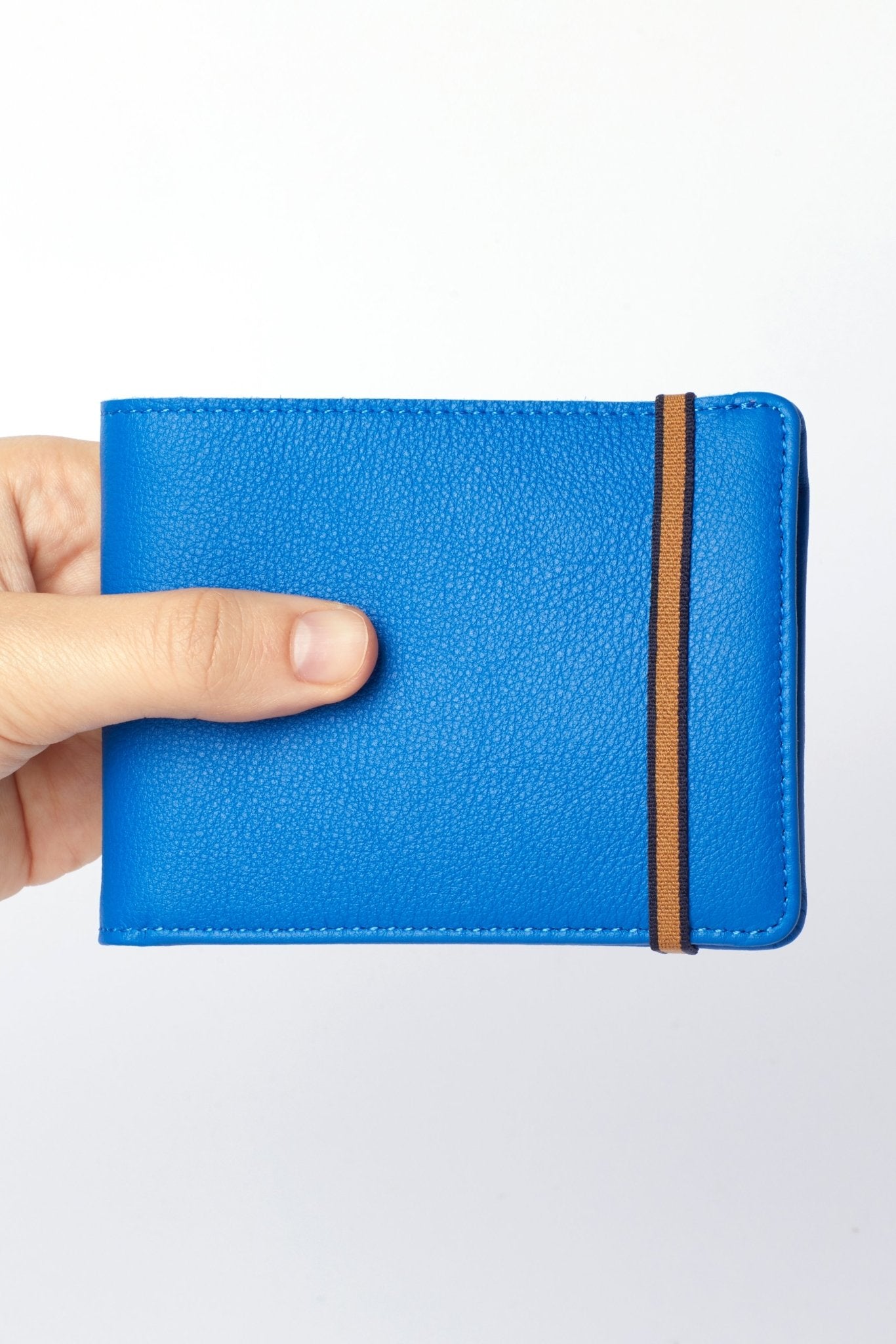 A man's hand is holding the Light Blue Minimalist Wallet with orange elastic closure on a white background - L'Atelier Global