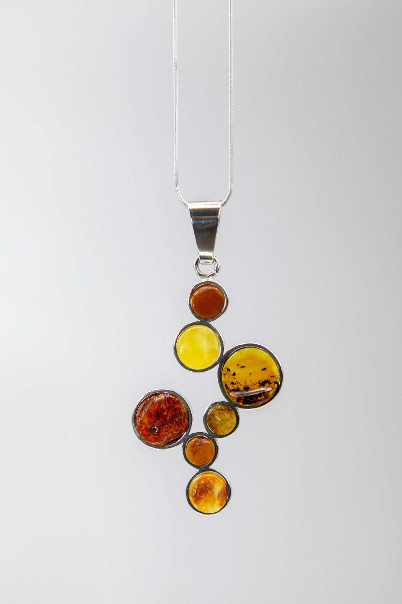 Multicolor Baltic Amber Stepping Stone Necklace hanging in front of a soft gray hued background- L'Atelier Global