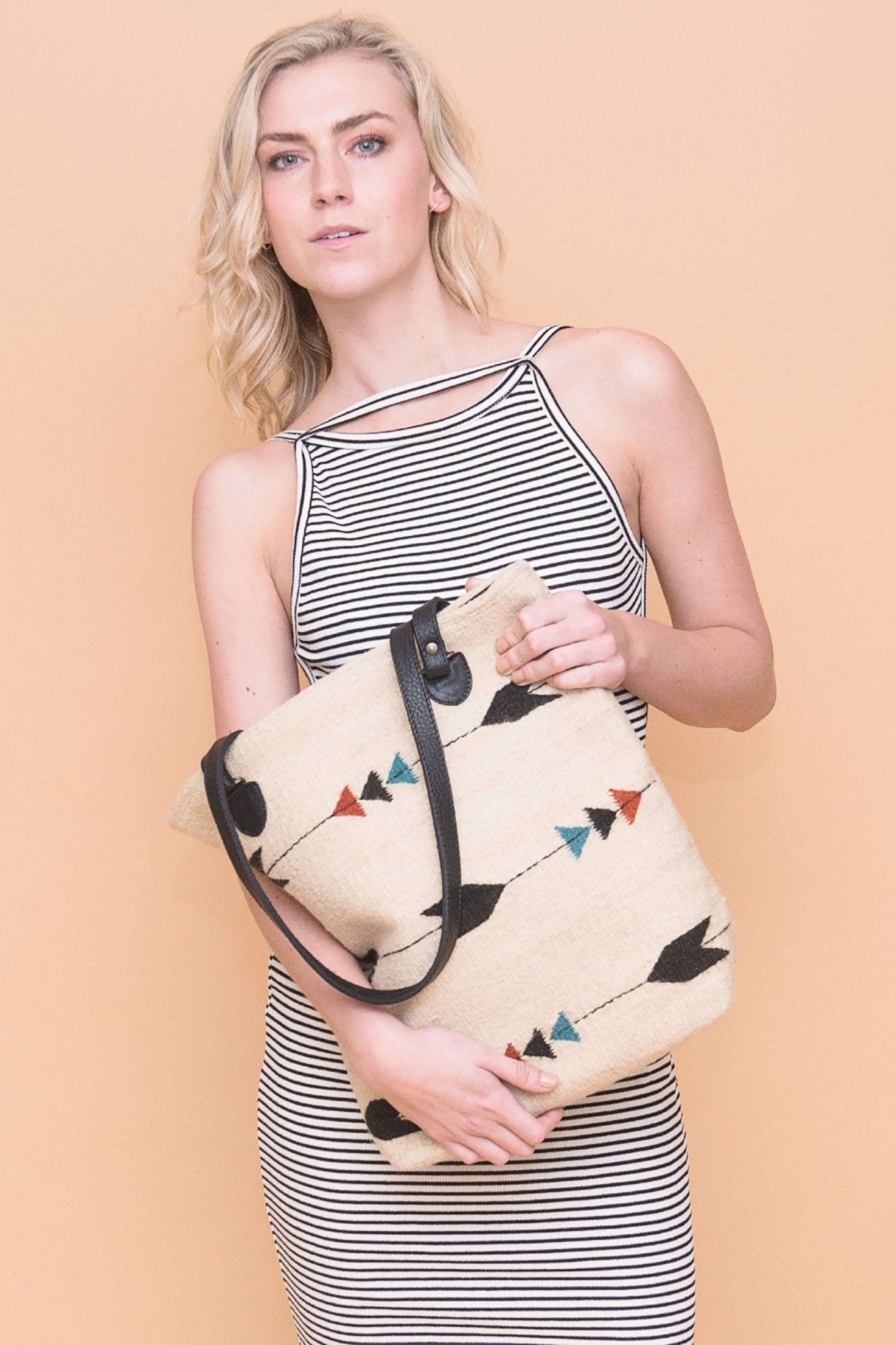 Obsidian Arrow Tote Bag is held by a female model wearing a blue and white striped sleeveless dress - L'Atelier Global