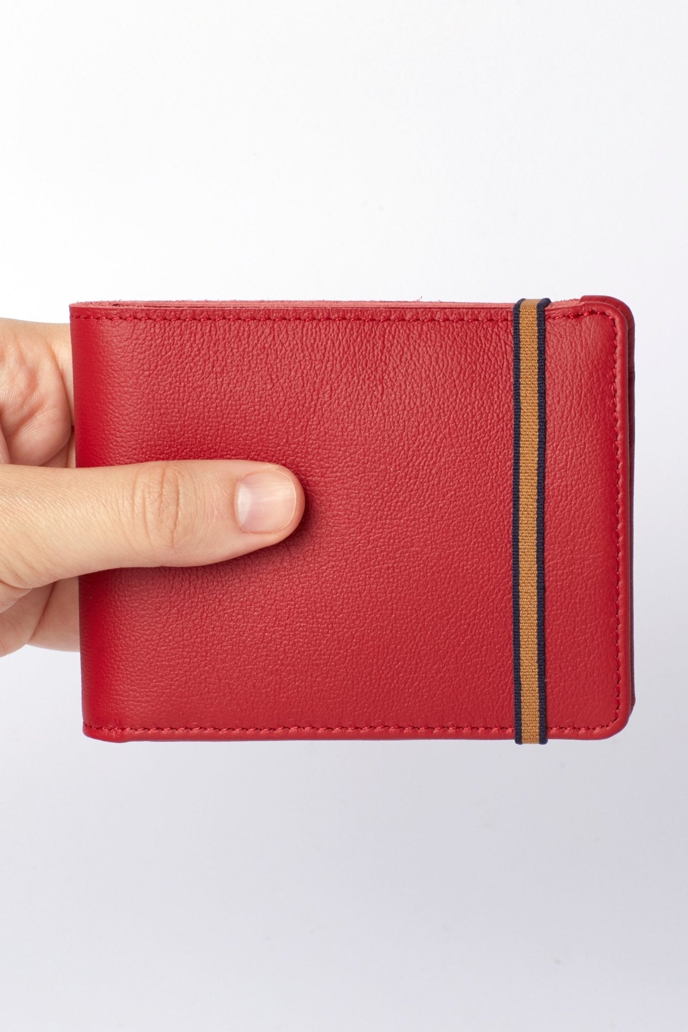 A man's hand is holding the Red Minimalist Wallet With Coin Pocket and gold and black elastic closure - L'Atelier Global