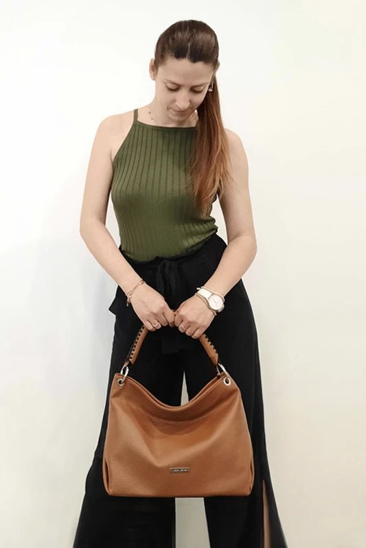 A female model wearing a dark olive tank and black pants holding the TL Bag Soft Leather Handbag in Cognac - L'Atelier Global