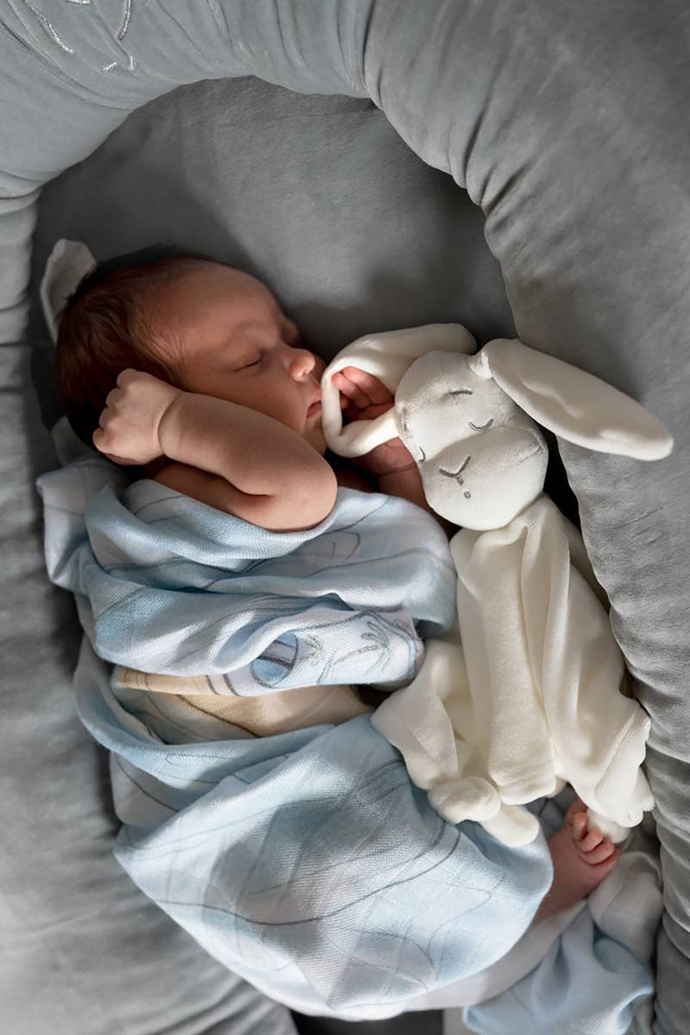 A baby is tucked safely inside the Velvet Baby Nest in Gray - L'Atelier Global