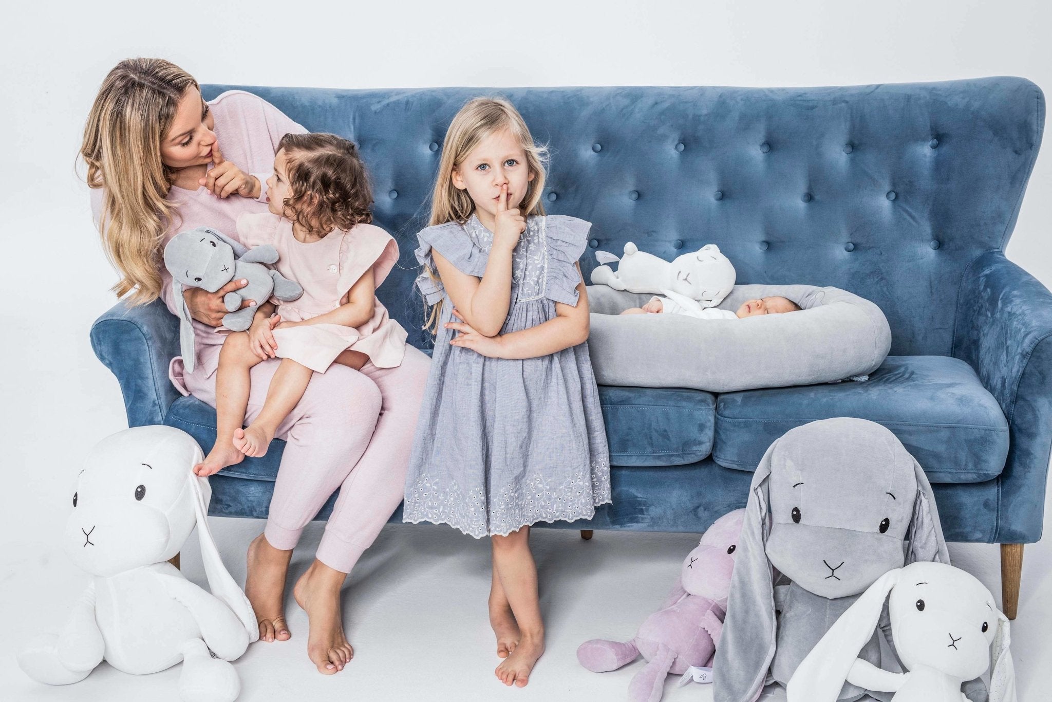 A mother and daughter are sitting on couch next to baby laying safely inside the Velvet Baby Nest in Blue - L'Atelier Global